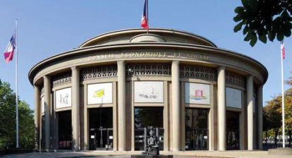 Bâtiment circulaire à colonnes, drapeaux français de part et d'autres, rond point en premier plan et ciel bleu