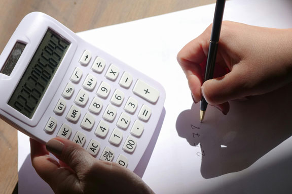 Photographie d'une main écrit sur une feuille blanche et l'autre tient une calculatrice