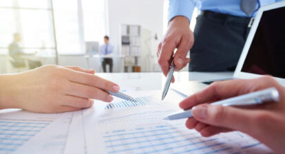 Gros plan sur les mains de trois personnes munis d'un stylo qui orientent leur pointe vers un document sur une table