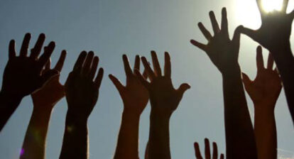 Photo de mains en contre-jour se levant sur fond de ciel bleu et soleil