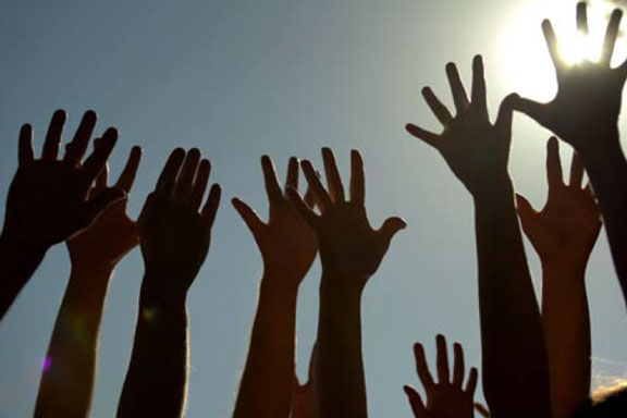 Photo de mains en contre-jour se levant sur fond de ciel bleu et soleil