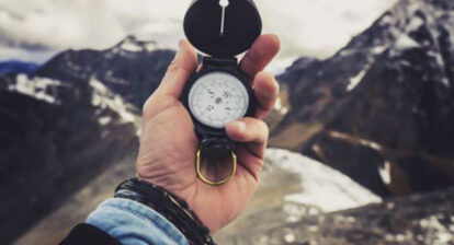 Boussole dans une main sur fond de paysage montagnard