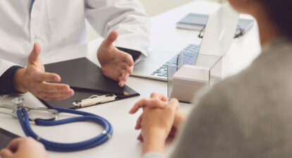 Photo cadrée sur les mains d'un médecin discutant avec deux personnes à un bureau
