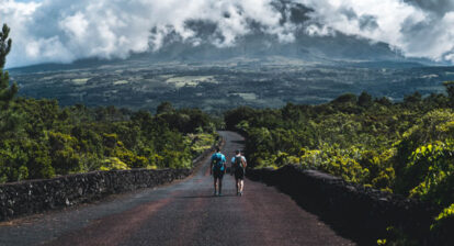 Deux marcheurs sur une route au milieu de la nature face à une montagne parsemée de nuages
